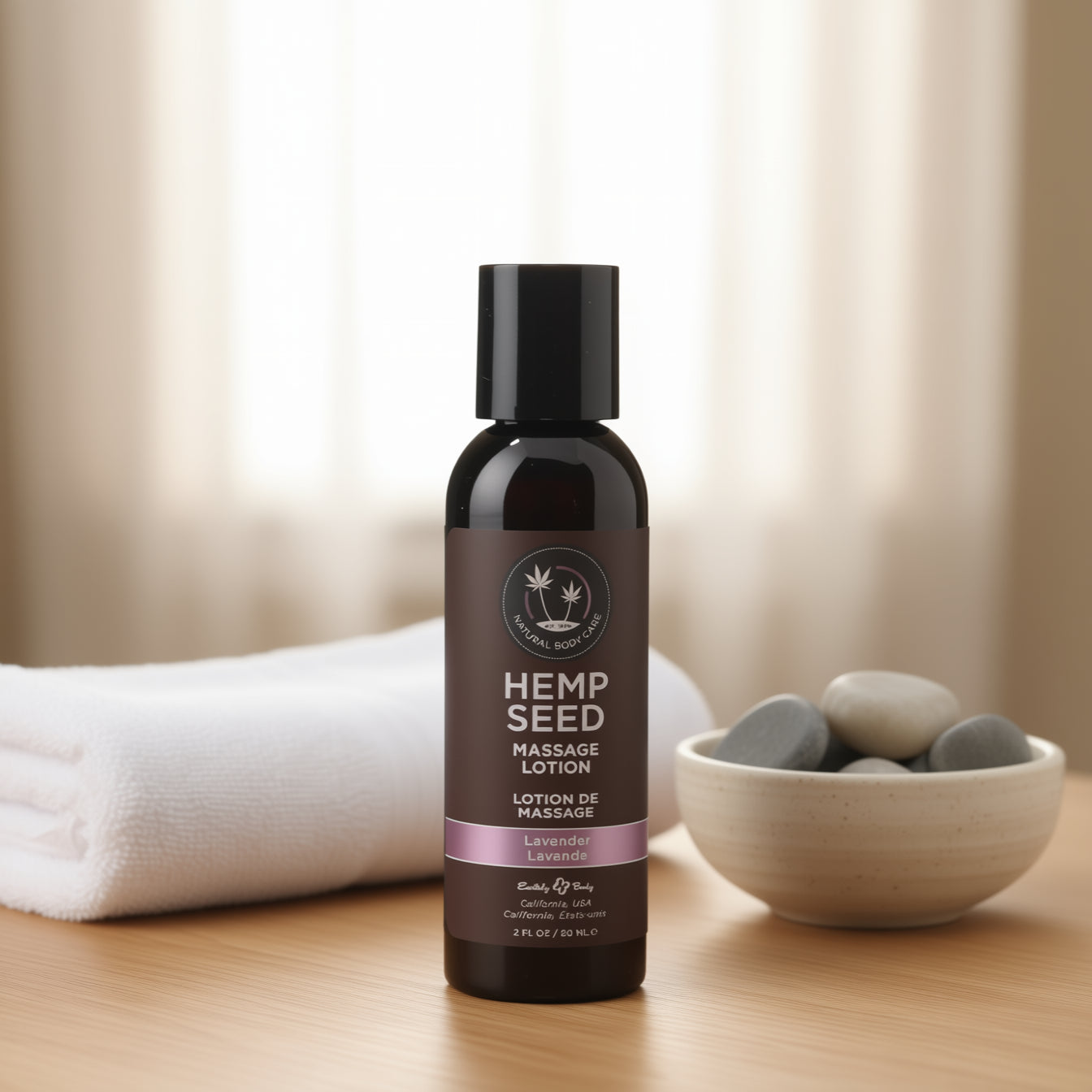 Bottle of hemp seed massage lotion on a wooden surface with a bowl of stones and a towel in the background.